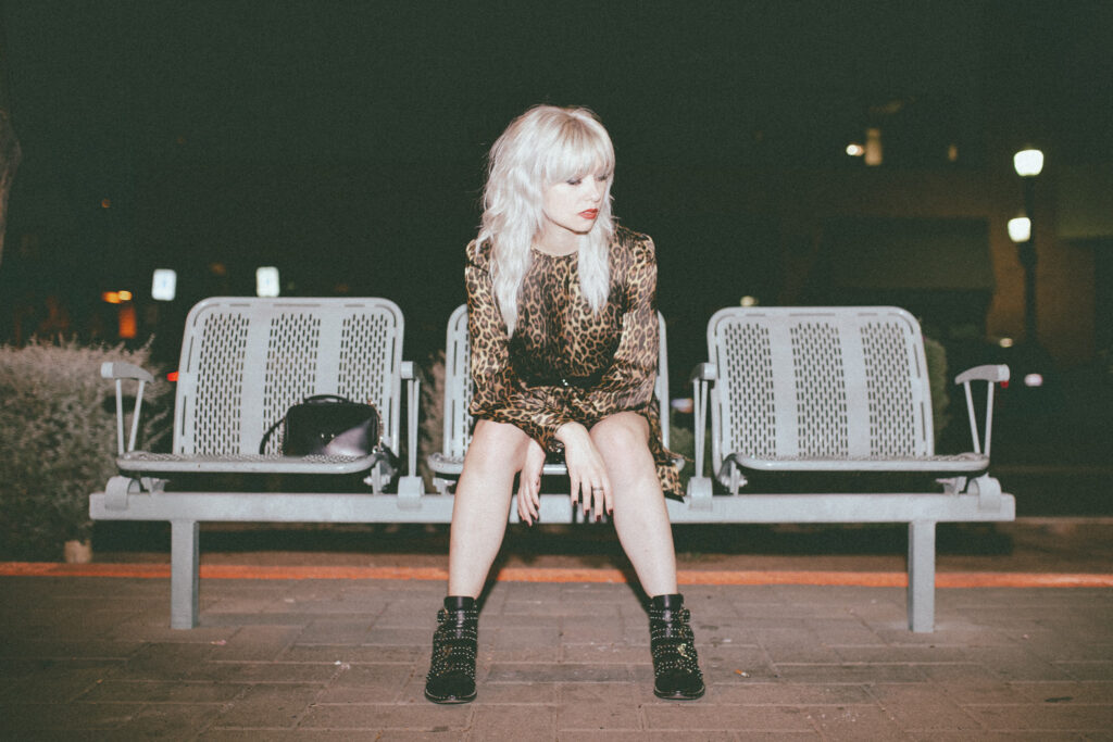 Trina in a leopard dress and boots sitting at a train station
